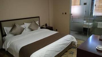 Hotelkamer met een bed, nachtkastje, douche met glazen wand en een klein bureau met stoel.