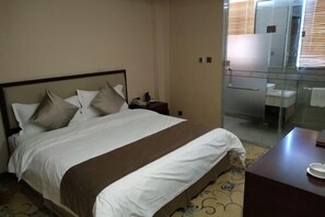Una habitación de hotel con una cama, una mesita de noche, una ducha con cerramiento de vidrio y un escritorio pequeño con una silla.