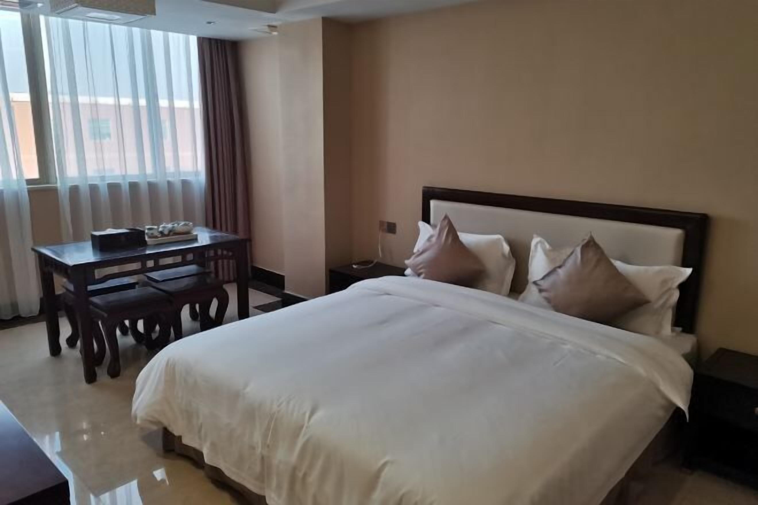 Une chambre d’hôtel avec un grand lit, une table de chevet, un bureau avec des chaises et une fenêtre avec des rideaux.
