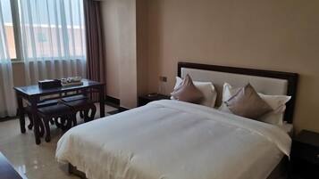 Een hotelkamer met een groot bed, een nachtkastje, een bureau met stoelen en een raam met gordijnen.