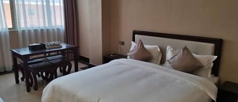 Une chambre d’hôtel avec un grand lit, une table de chevet, un bureau avec des chaises et une fenêtre avec des rideaux.