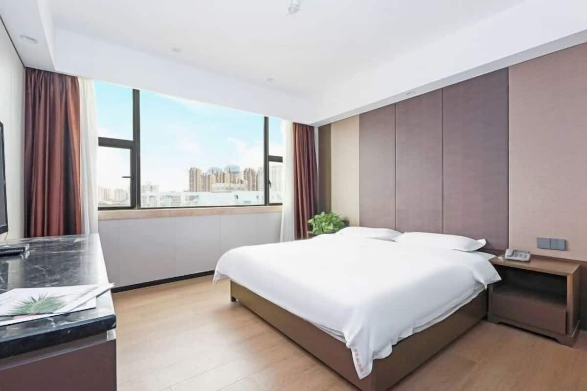 Une chambre d’hôtel moderne, dotée d’un grand lit, d’un bureau et offrant une vue sur les toits de la ville grâce à de grandes fenêtres.