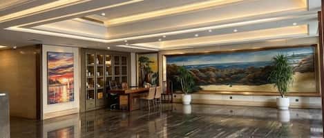 A lobby with a polished marble floor, a reception desk, a large painting, and a bookshelf.