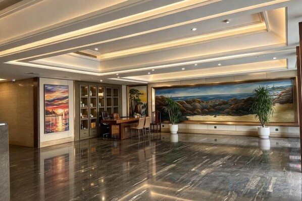 A lobby with a polished marble floor, a reception desk, a large painting, and a bookshelf.