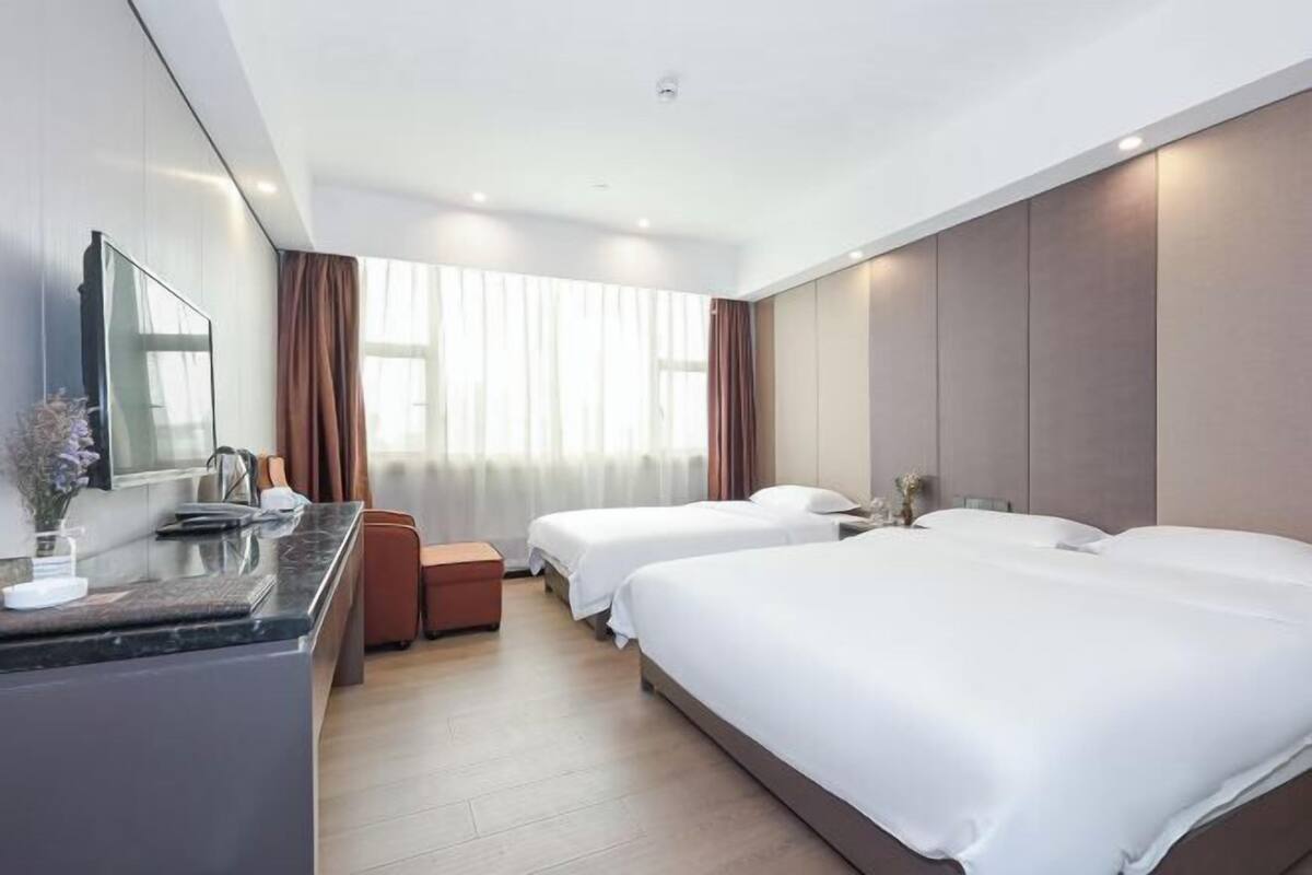 Une chambre d’hôtel avec un lit, un bureau, une chaise, un miroir et une fenêtre avec des rideaux.