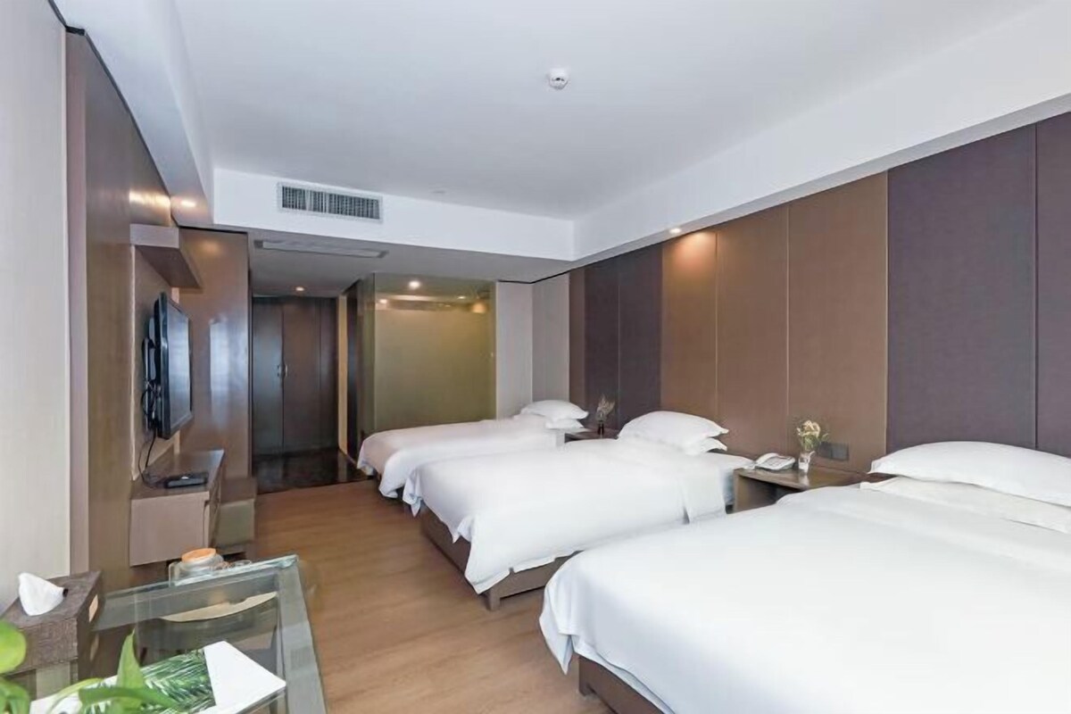 Hotelkamer met drie bedden, een televisie, een bureau en een glazen scheidingswand.