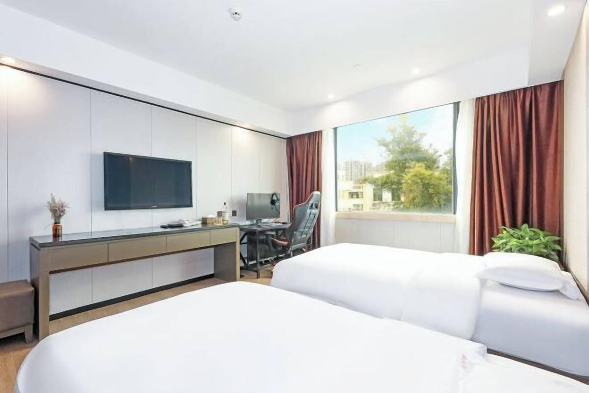 Une chambre d’hôtel moderne équipée de deux lits, d’un bureau, d’une télévision à écran plat et d’une grande fenêtre avec des rideaux.