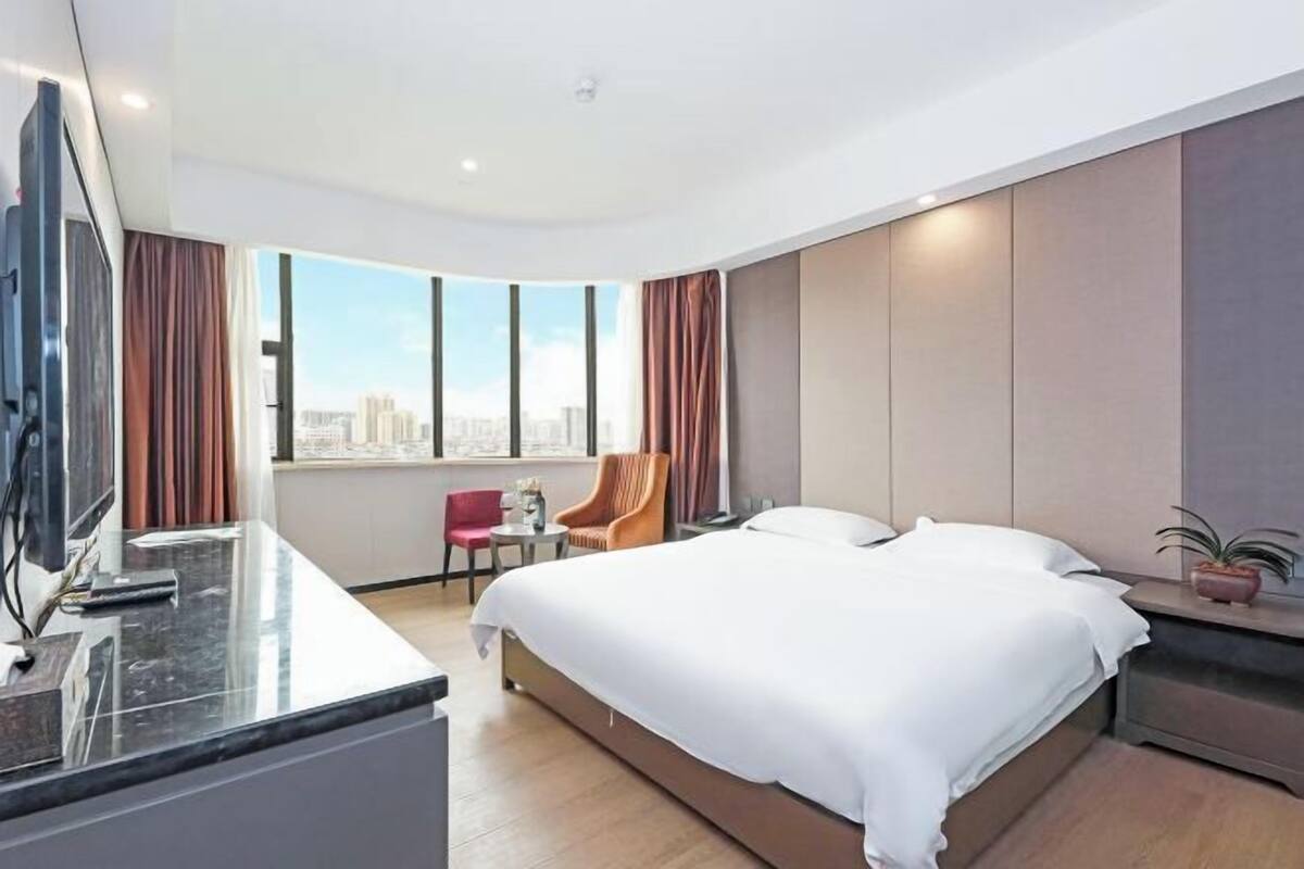 Une chambre d’hôtel moderne dotée d’un grand lit, d’un bureau avec un téléviseur à écran plat, d’une chaise et offrant une vue sur la ville.