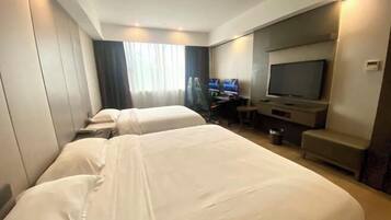 A hotel room with two beds, a desk, a TV, and a seating area.