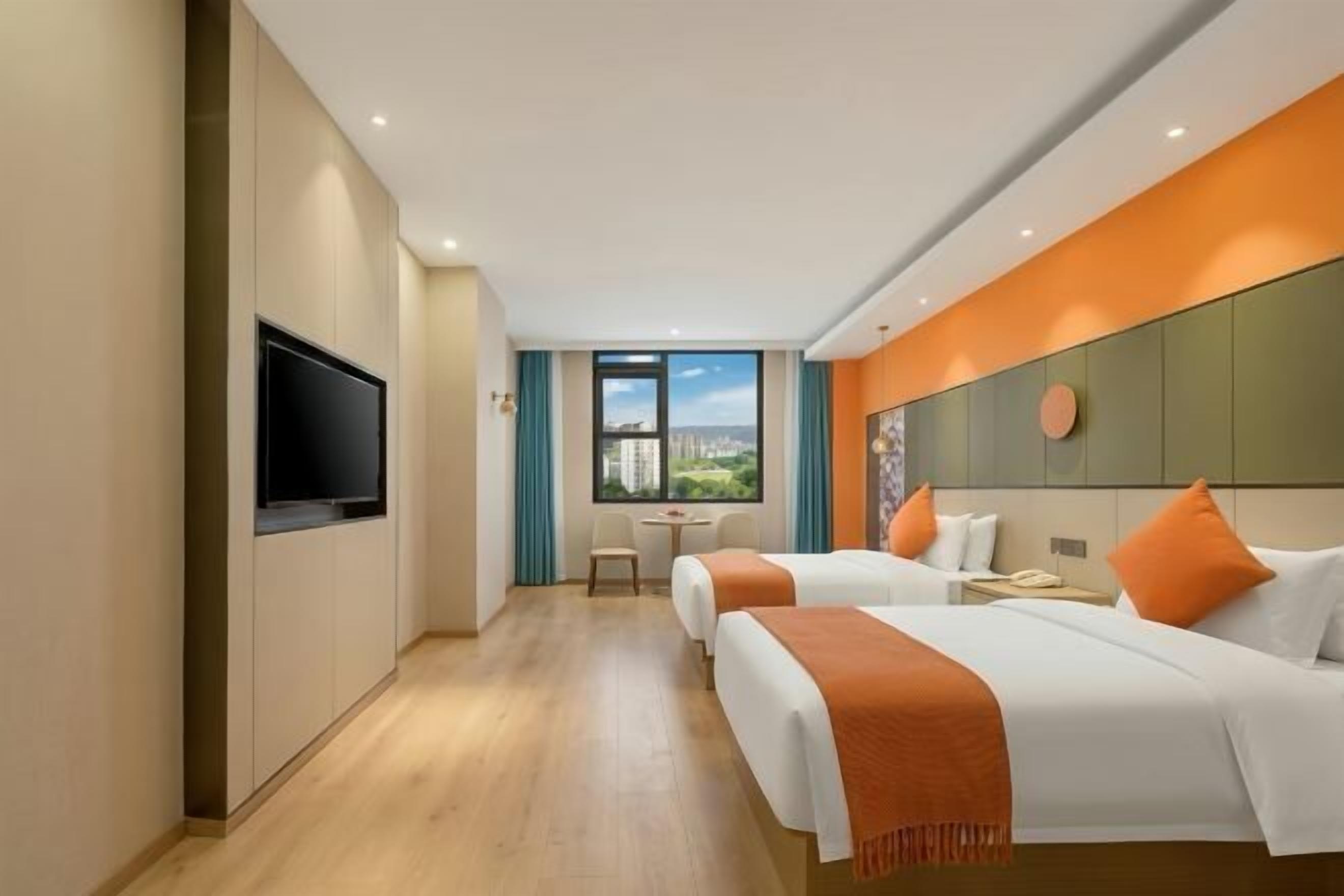 A hotel room with two beds, a TV, a desk, and a window with a city view.