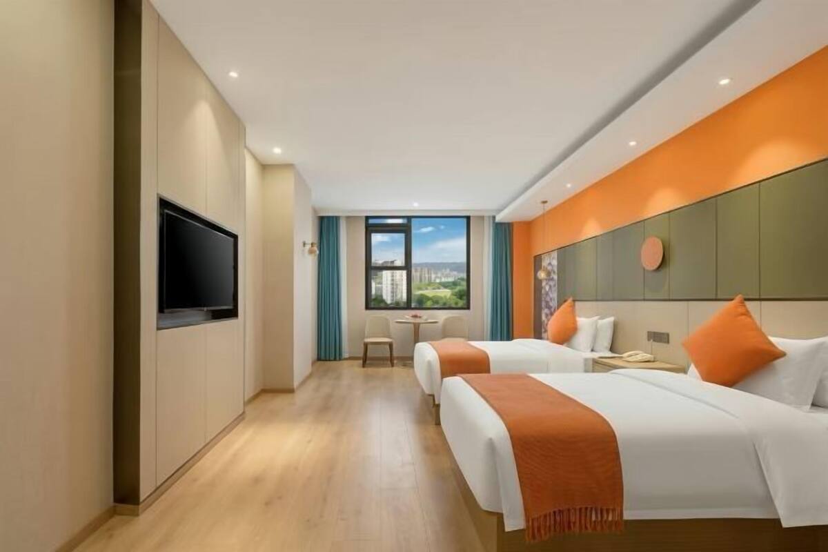 A hotel room with two beds, a TV, a desk, and a window with a city view.