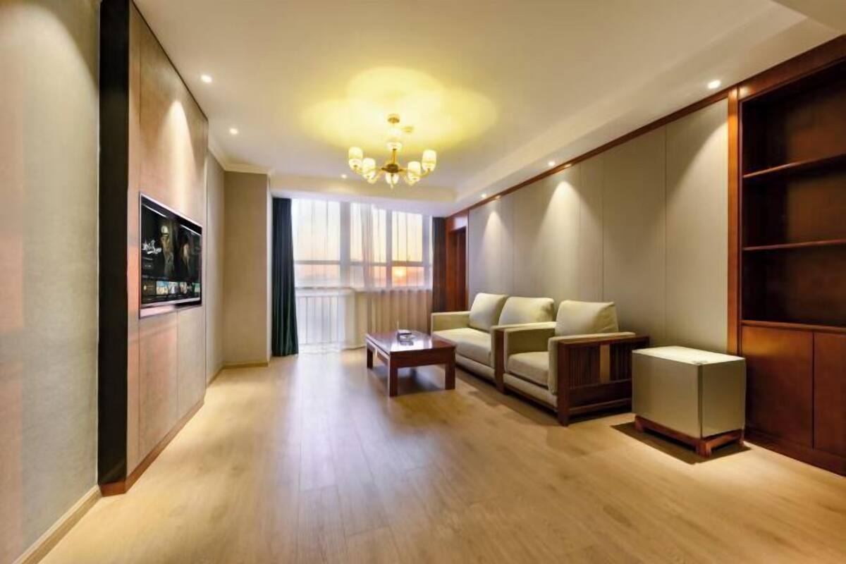 A spacious living room with a wooden floor, a sofa set, a coffee table, and a television on the wall.