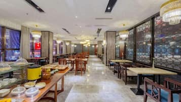 A spacious dining area with multiple tables and chairs, a buffet line with various food items, and decorative wall panels.