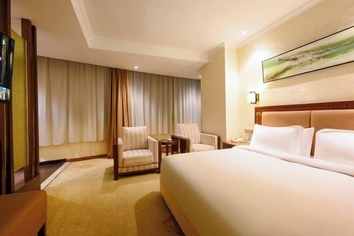 A hotel room with a large bed, two armchairs, a small table, and a painting on the wall.