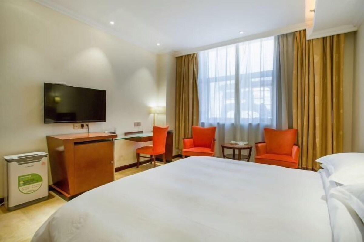 Habitación de hotel con una cama grande, un escritorio con una silla, un televisor y dos sillones naranjas.