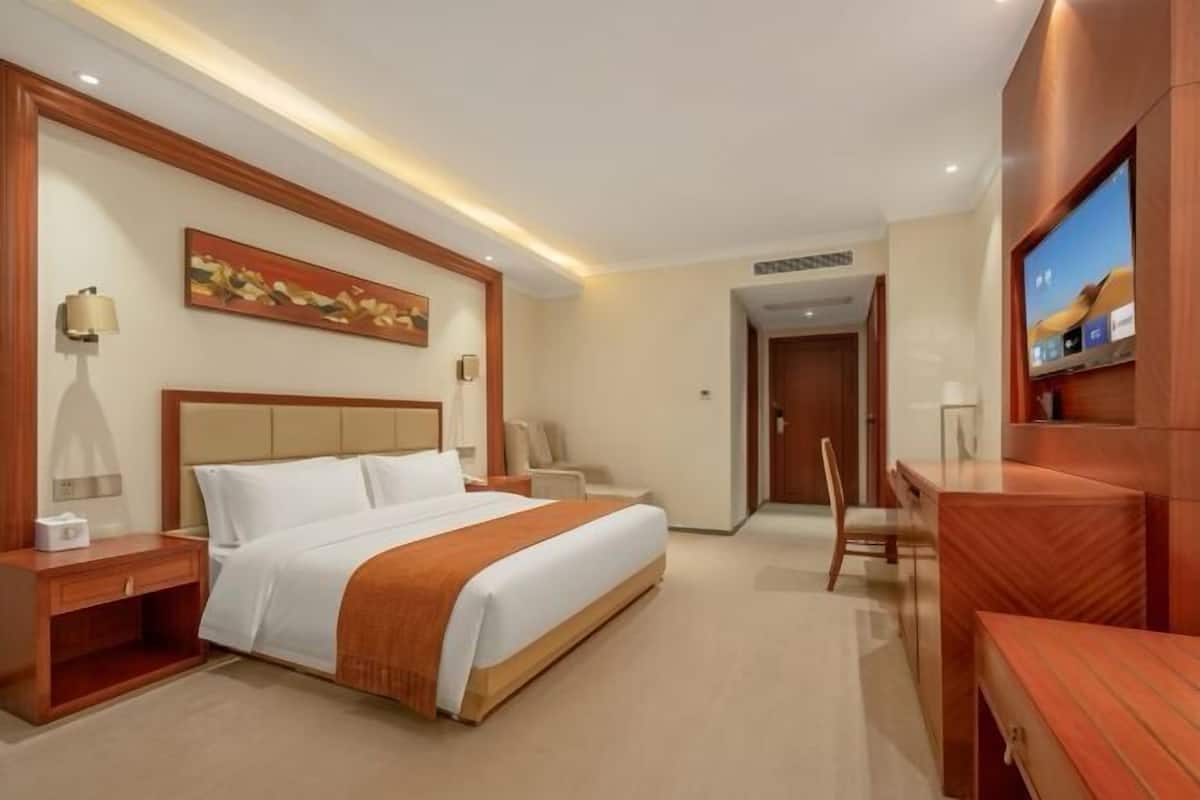 A hotel room with a bed, bedside tables, a desk, a chair, a television, and a painting on the wall.