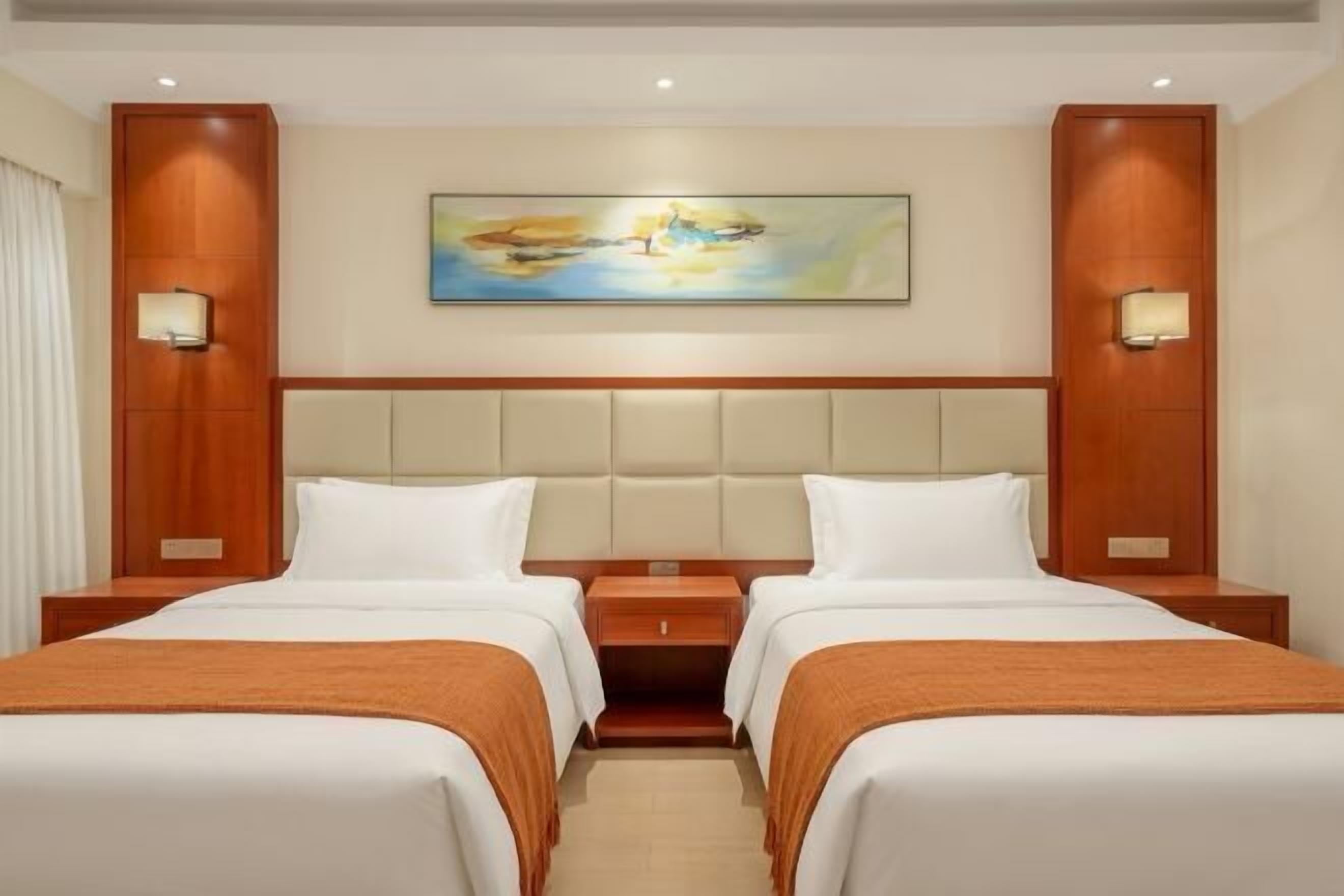 A hotel room with two beds, a large painting on the wall, and two bedside lamps.