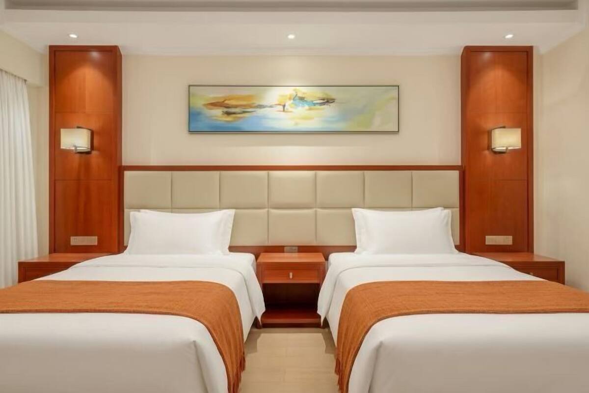 A hotel room with two beds, a large painting on the wall, and two bedside lamps.