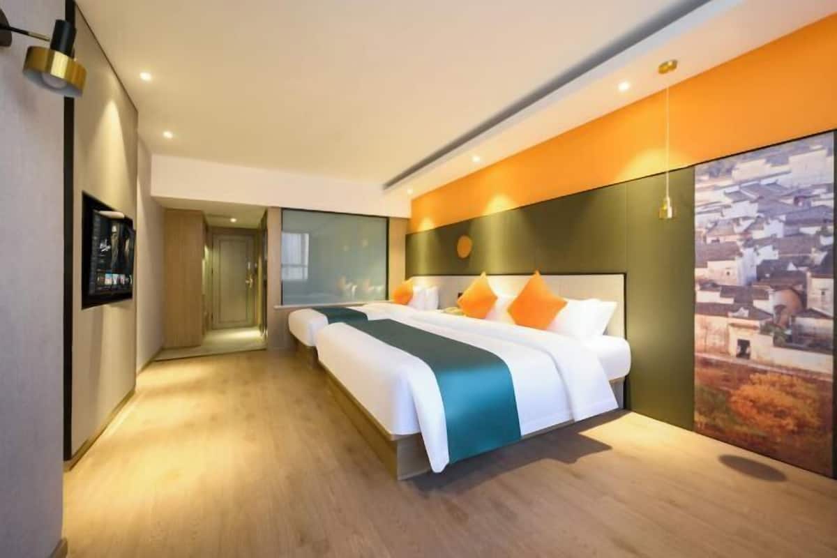 A modern hotel room with a large bed, a view of a cityscape, and a hallway leading to another room.