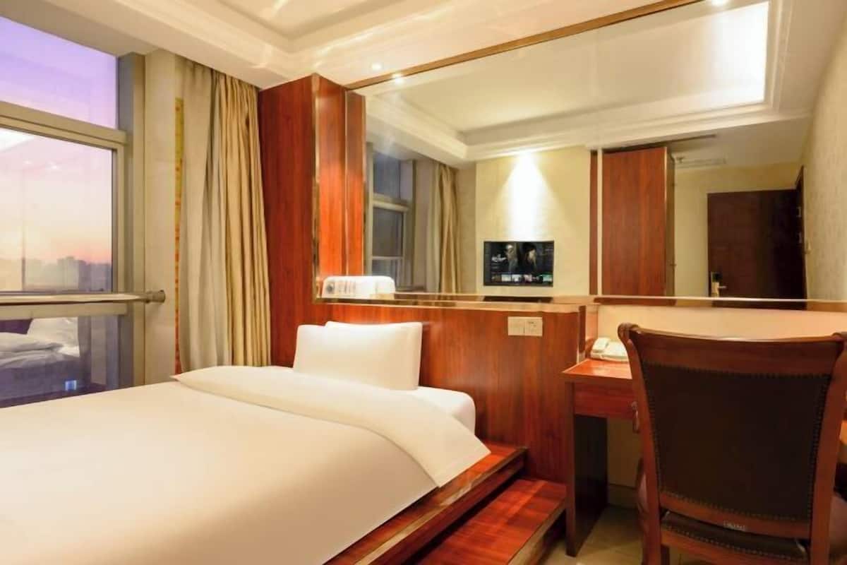 A hotel room with a bed, a desk, a chair, a TV, and a window with curtains.