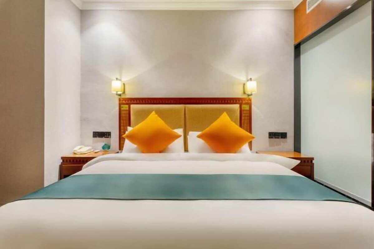 Habitación de hotel con una cama grande, dos mesitas de noche, un cabecero de madera y dos lámparas de pared.