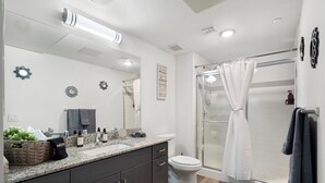 Ein modernes Badezimmer mit einem großen Spiegel, dunklen Schränken, einer Dusche mit Glastür und einem Waschbecken mit verschiedenen Pflegeprodukten.