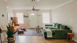 Sala de estar com piso de madeira, um sofá verde, um sofá de couro marrom, um ventilador de teto e uma porta com janela.