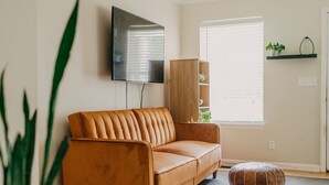 Sala de estar com sofá, pufes, planta em vaso e televisão na parede.
