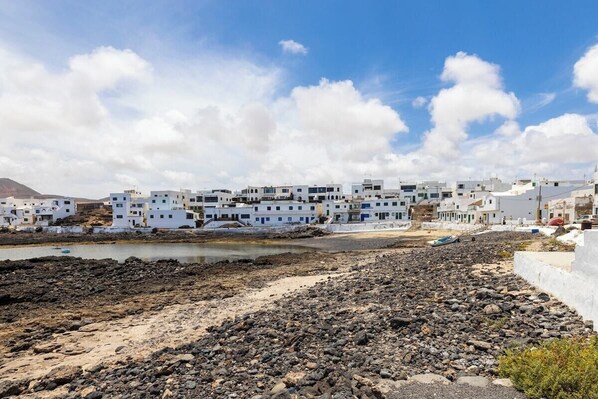 Un pueblo costero con edificios blancos, playa de roca y cielo despejado.