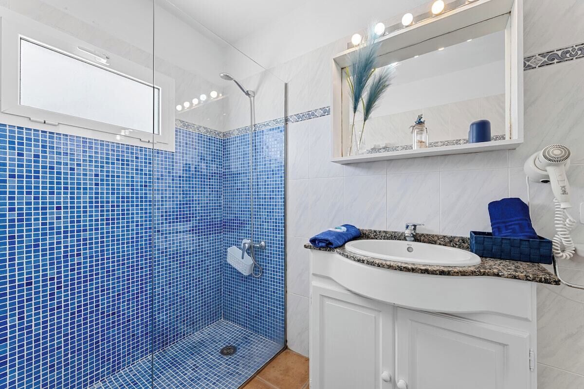 Un bany amb dutxa revestida de rajoles blaves, un lavabo blanc i un mirall a sobre.