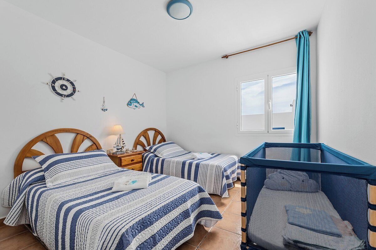 A bedroom with two beds, a window with a view, a clock, and a small table with a lamp.