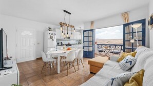 A modern living space with a dining area, kitchen, and a large window offering a view of the landscape.