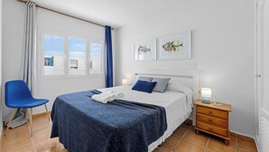 A bedroom with a bed, a chair, a nightstand, and a window with curtains.