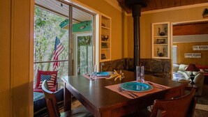 A dining area with a wooden table set for two, a stone fireplace, and a view of the outdoors through a sliding glass door. - Rustic Charm Meets Modern Comfort (Groveland)