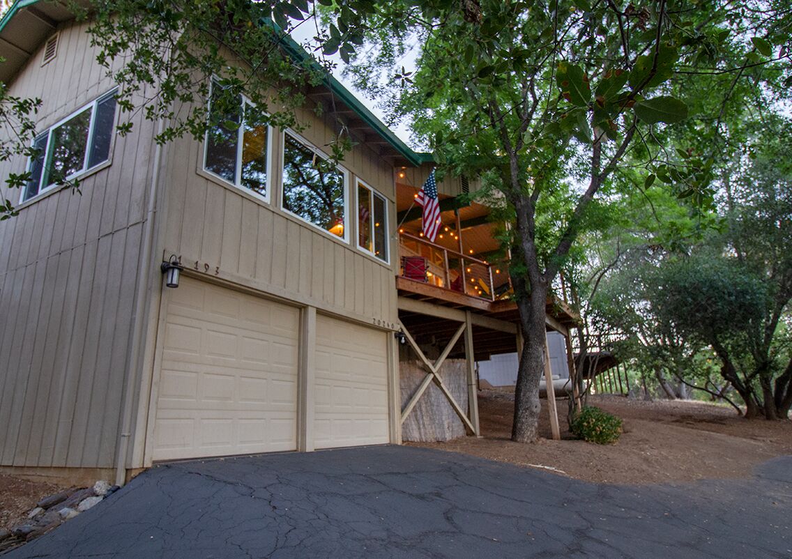 A two-story building with a garage, a balcony with an American flag, and a tree in front.