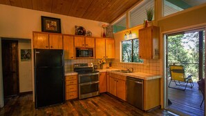 A kitchen with wooden cabinets, a black refrigerator, a microwave, a stove, and a sink. - Rustic Charm Meets Modern Comfort (Groveland)