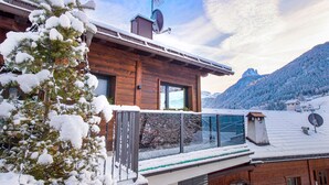 Een houten hutje met een glazen balkon, omgeven door met sneeuw bedekte bomen en bergen.