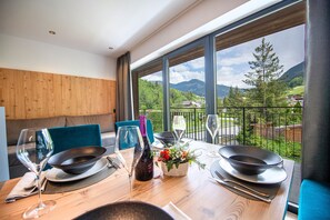 Spiseområde med et træbord dækket til to, udsigt til bjerge og en balkon med gelænder.