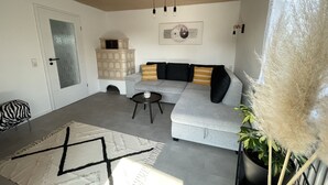 A living room with a grey sofa, a small round table, a white rug with black patterns, a door with frosted glass, and a wall-mounted light fixture. - Ferienwohnung Heidi (Rielasingen-Worblingen)