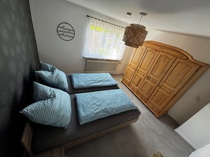 A bedroom with a bed, pillows, a wardrobe, a radiator, and a window with curtains.