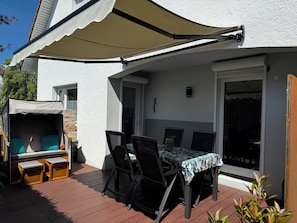 Een terras met een tafel en stoelen, een overdekte zithoek en een schuifpui.