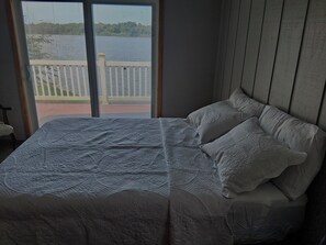 A bedroom with a bed, two pillows, and a view of a balcony with a railing. - Welcome to this charming lake house beautifully located on Lake Matanzas. (Havana)
