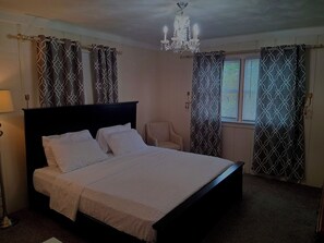 A bedroom with a large bed, a chandelier, patterned curtains, and a window with blinds.