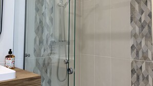 Une douche fermée par des parois en verre, dotée d’un pommeau de douche à main et d’un panneau de commande fixé au mur.