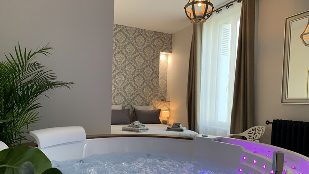 Une salle de spa équipée d’un jacuzzi, d’un miroir, d’une plante et d’une fenêtre avec des rideaux.