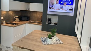 Une cuisine moderne avec des meubles blancs, un plan de travail en bois, un four à micro-ondes, une machine à café et un téléviseur diffusant une émission de cuisine.