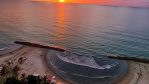 A beach with a stone wall and umbrellas, a sunset over the ocean, and people on the shore. - NEW Apartment Frente a la Playa Bocagrande (Cartagena de Indias)