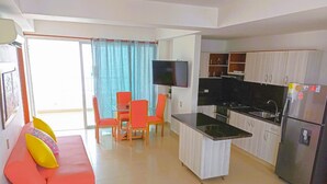 A modern kitchen with a built-in oven and a refrigerator, a dining area with a glass table and orange chairs, and a living area with a pink sofa and yellow cushions. - NEW Apartment Frente a la Playa Bocagrande (Cartagena de Indias)