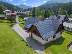 A rural house with a sloped roof, surrounded by a cobblestone driveway and a grassy area.
