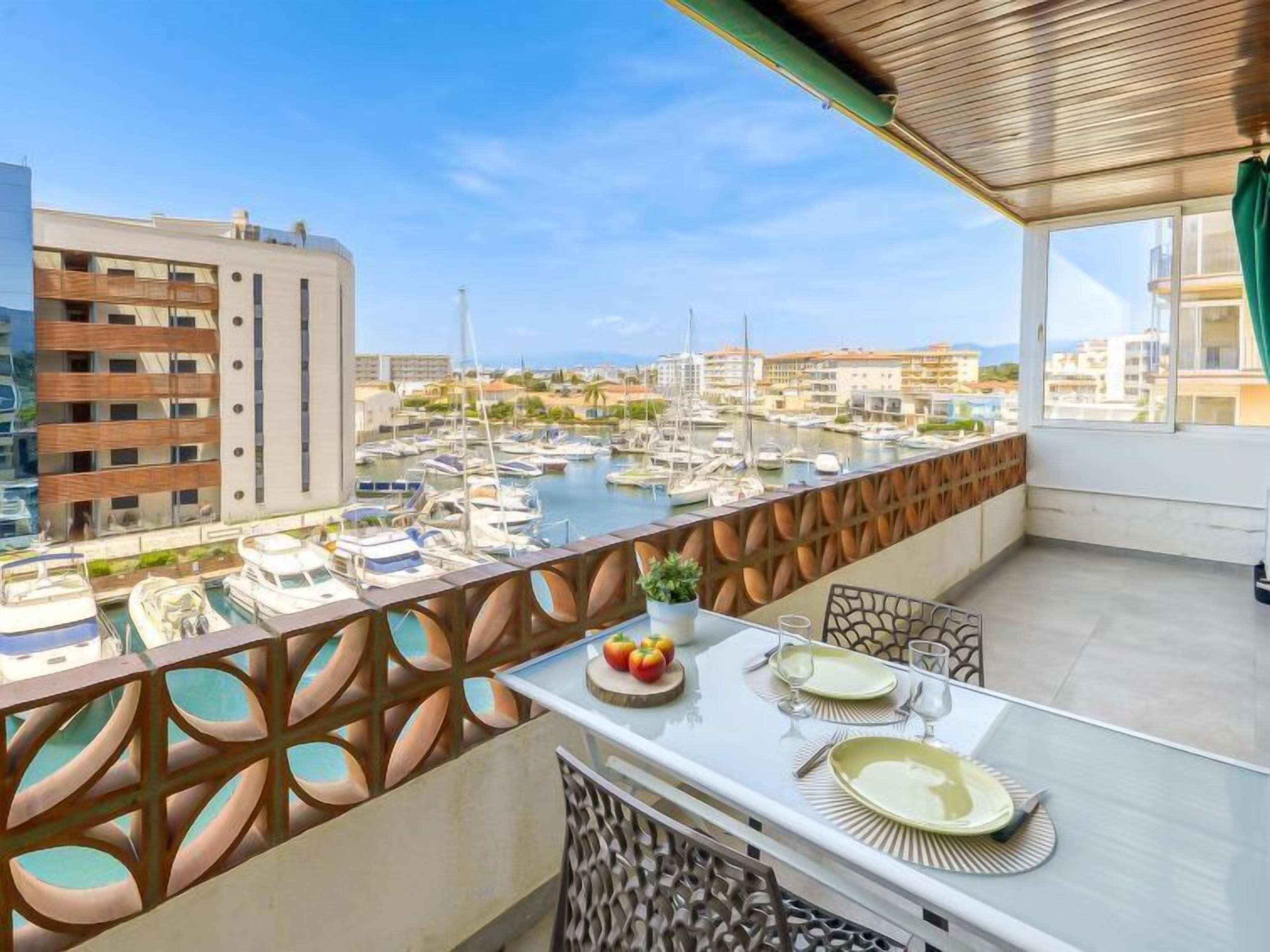 A balcony with a table set for dining, overlooking a marina with boats and buildings.